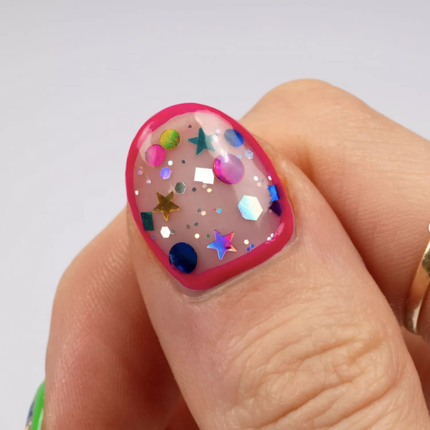 Un pouce avec des confettis encapsulés, encadrés de vernis à ongles rose