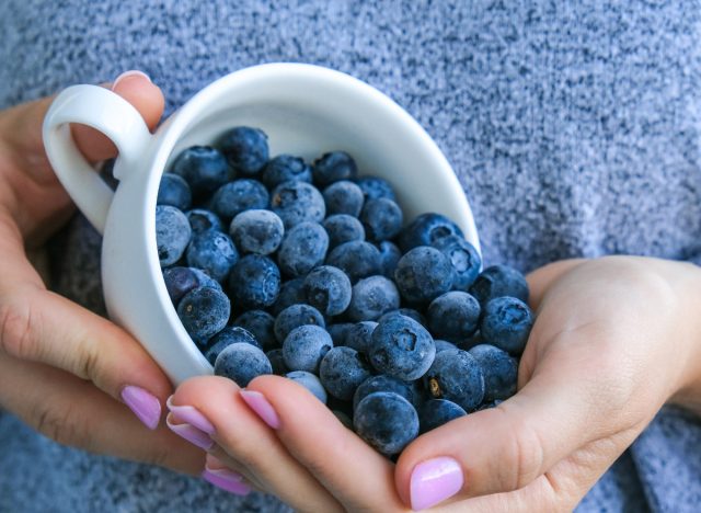 femme en gros plan versant une tasse de myrtilles dans la main, des aliments pour brûler la graisse du ventre