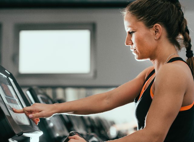 femme à la salle de sport soulevant l'inclinaison du tapis roulant