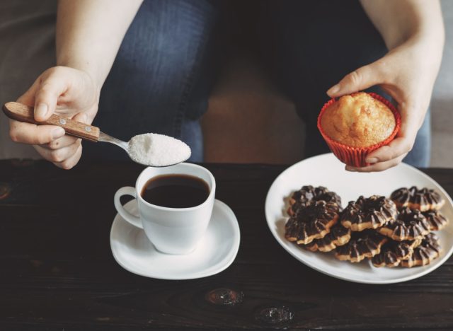 femme versant du sucre dans le café, tenant un muffin au-dessus d'une assiette de biscuits