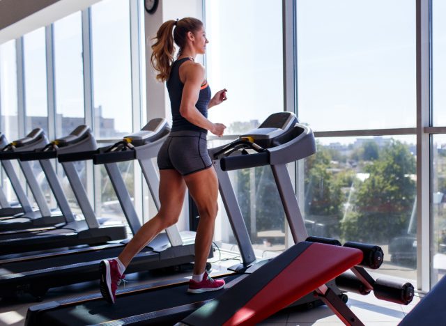 femme faisant de l'exercice pour brûler les graisses sur un tapis roulant devant les fenêtres de la salle de sport